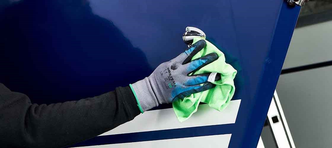 Person wearing work gloves wipes blue and white hull surface with a green microfibre cloth. Used as inspiration for the article topic ‘How to take care of your boat’