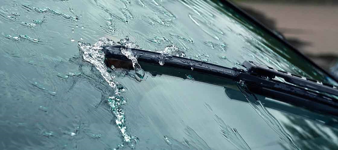 Nærbillede af forrudeviskere i funktion, der fjerner regnvand fra bilens forrude under kørsel.