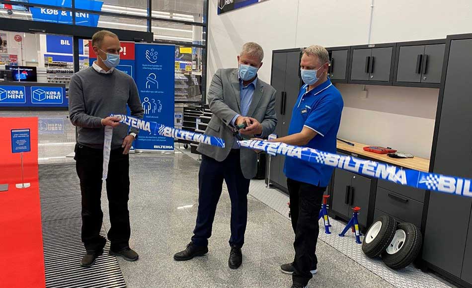 Tre mænd med mundbind deltager i officiel åbning af Biltema-butik, hvor der klippes blå Biltema-bånd over i butikslokale