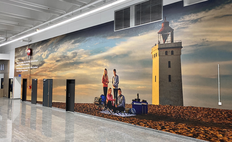 Stor vægudsmykning i Biltema-butik forestillende familie på strand med picnic tæt ved Rubjerg Knude Fyr i solnedgang