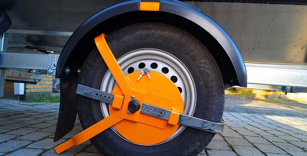 Close-up of trailer wheel with attached orange wheel lock for anti-theft protection.