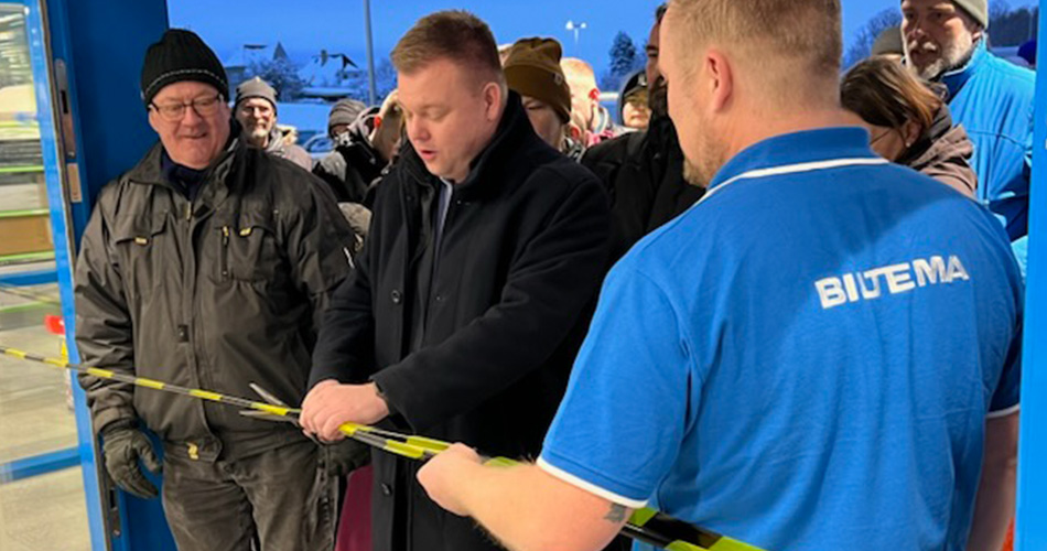 En mand klipper det gule bånd under åbningsceremoni ved Biltema-butik, omgivet af medarbejdere og kunder
