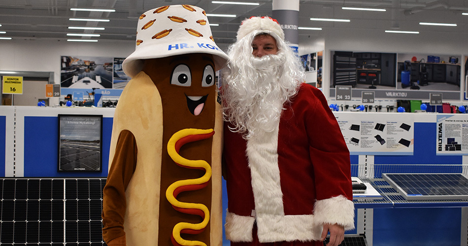 Biltemas maskot i pølse-kostume står smilende sammen med en mand klædt ud som julemand i butikslokalet