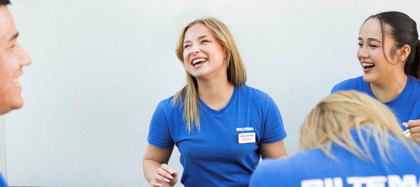 Fire Biltema-medarbejdere i blå skjorter griner sammen i en pause eller under et møde.