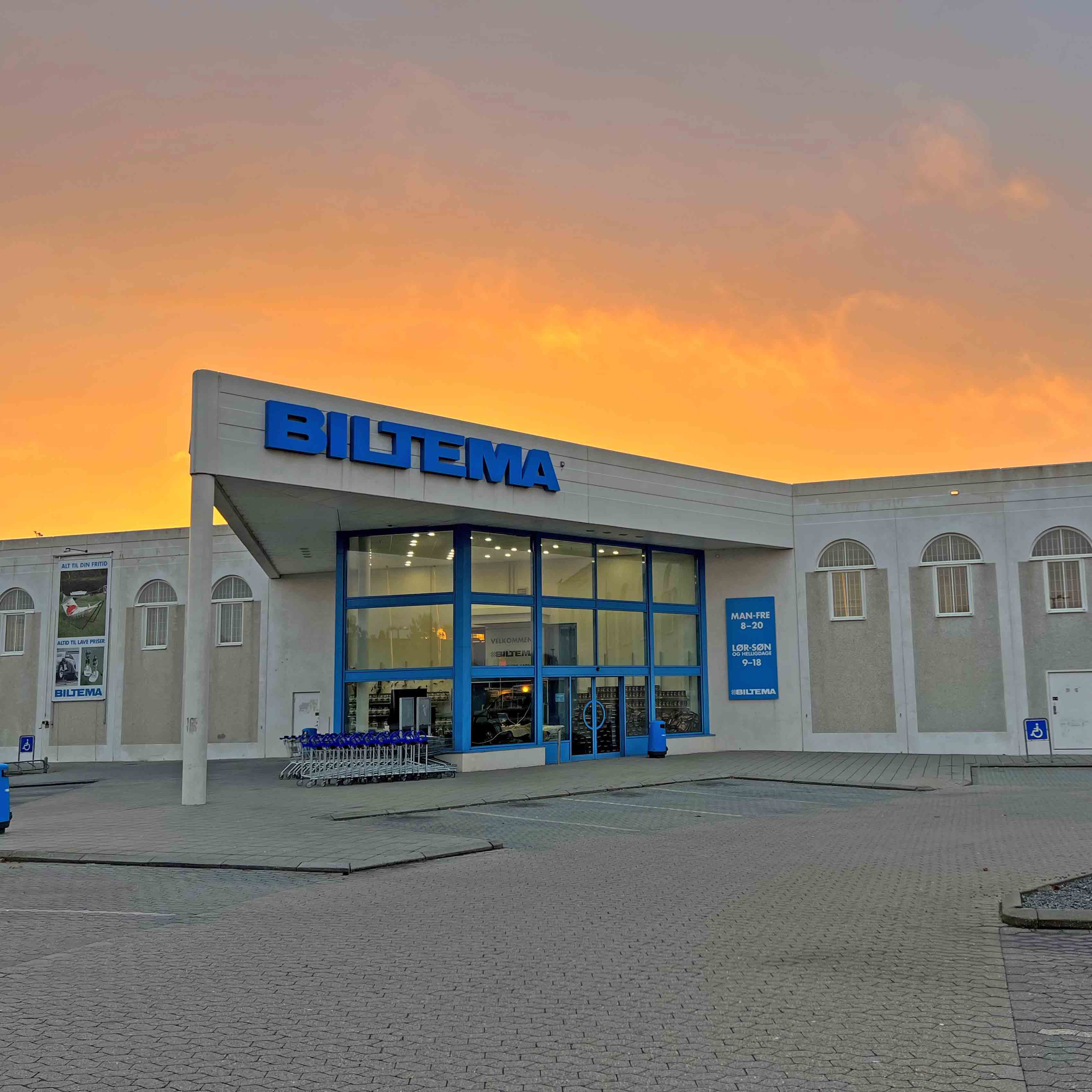 Biltema-varehus med blåt logo fotograferet i solnedgang med orangegul himmel.