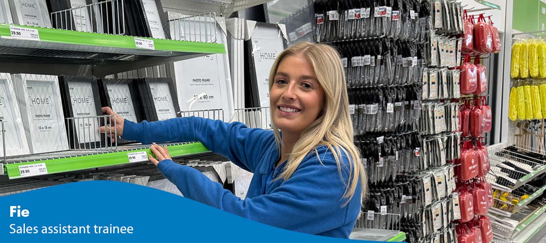 Employee in a Biltema warehouse by shelves with picture frames and products.