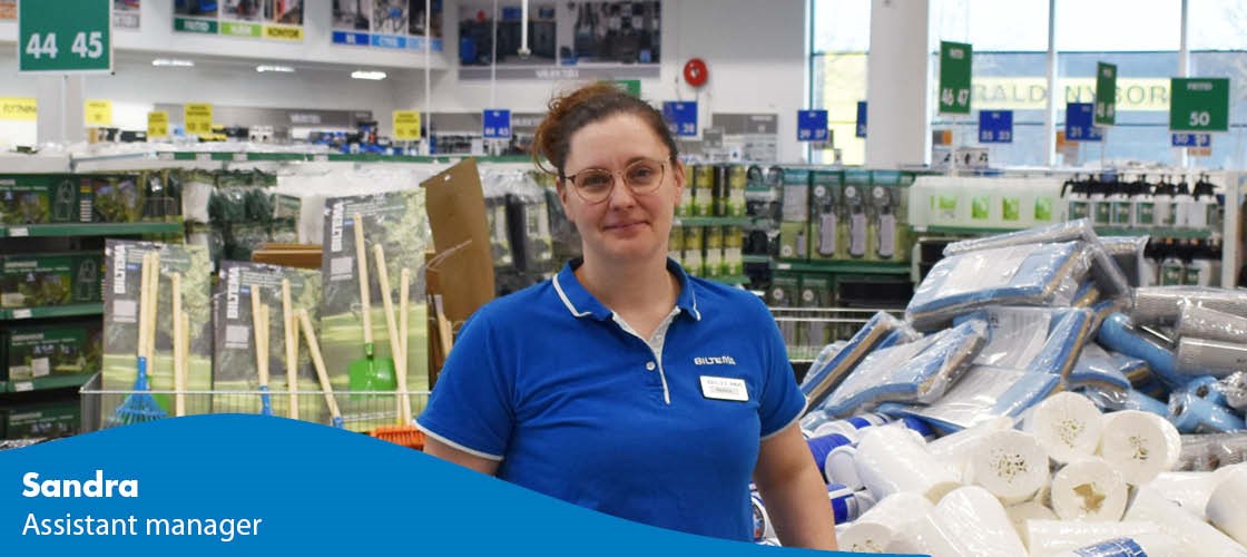 Female employee in a Biltema store in front of shelves with products and signs.