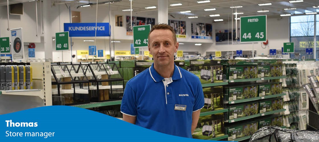 Male employee in a Biltema store with signs for customer service and the leisure department.