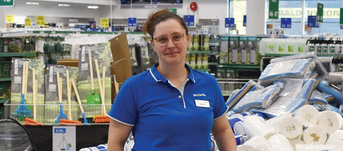 Female employee in a Biltema store in front of shelves with products and signs.
