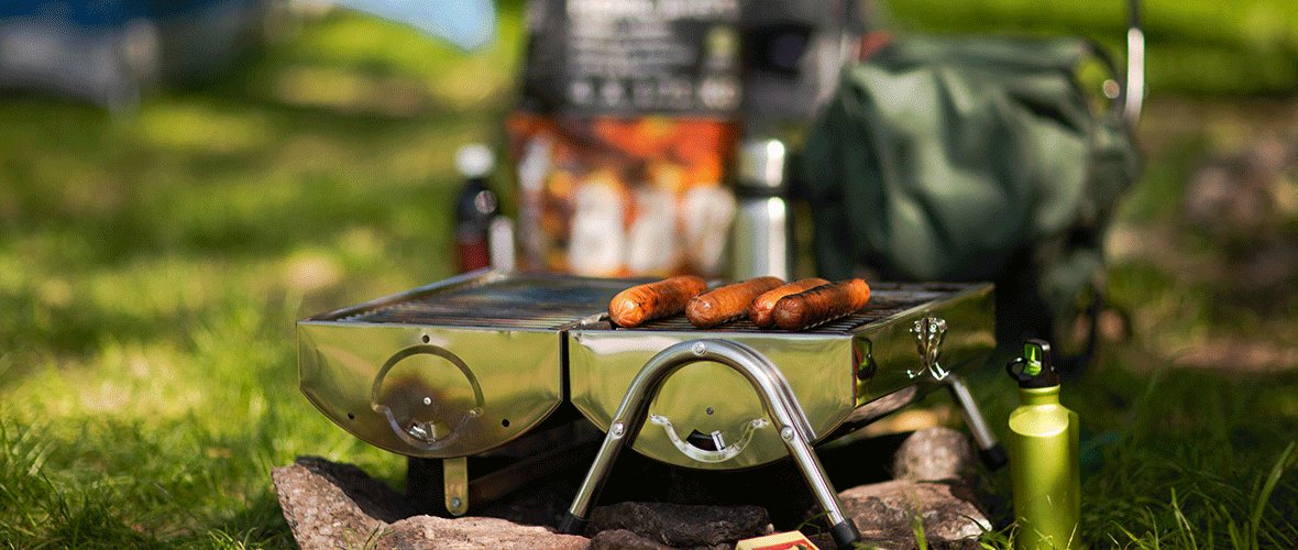 Bærbar camping grill med grillpølser tilberedt udendørs på en campingplads.