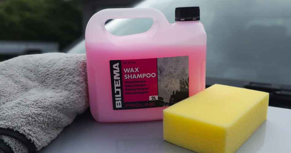 Biltema microfibre cloth, wax shampoo and cleaning sponge lie on the bonnet of a car, ready for exterior cleaning and washing.
