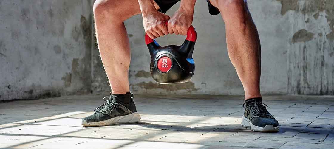 En person udfører en squat med en 8 kg kettlebell på et lyst træningsgulv.