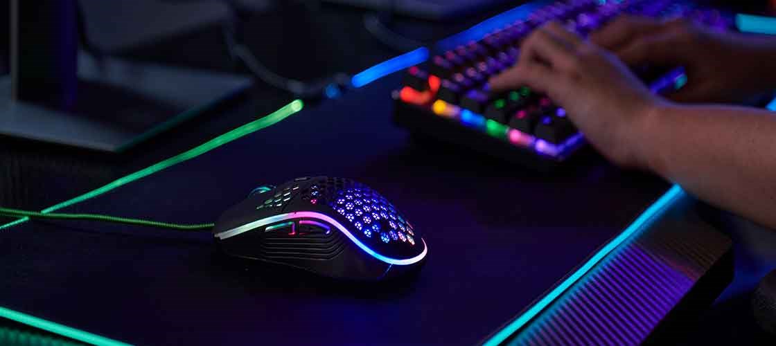 Gamingmus med RGB-belysning på et skrivebord ved siden af et oplyst gamingtastatur.