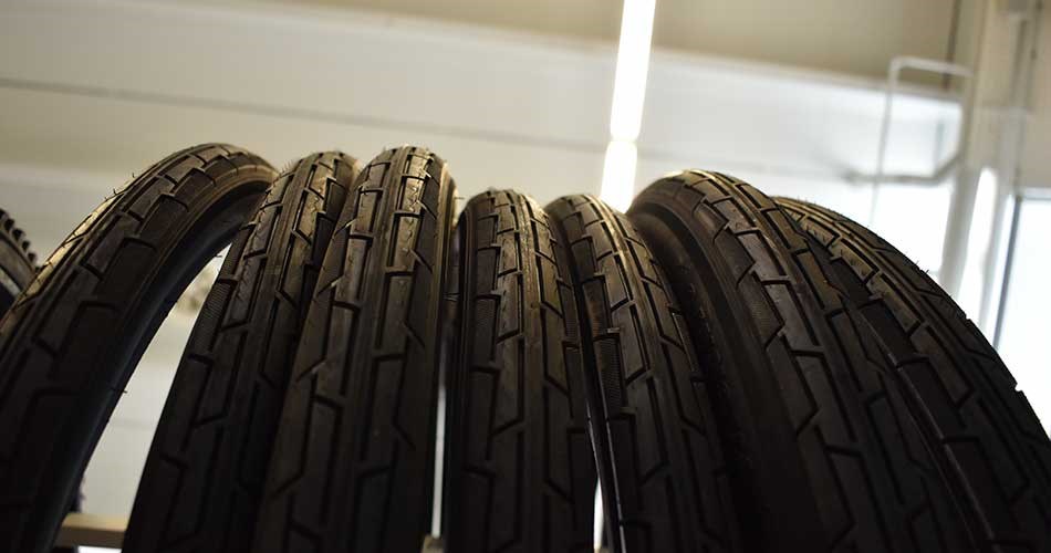 Row of vertically stored bicycle tyres with distinct tread pattern, set up indoors under ceiling lighting.