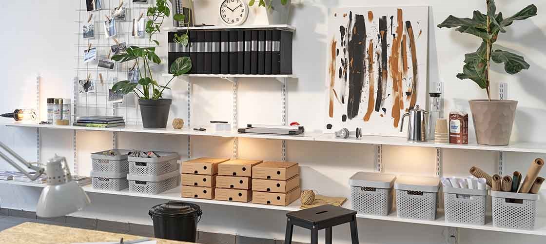 Vægopbevaring med hylder, opbevaringskasser, planter og kontorartikler i et kreativt arbejdsrum og hjemmekontor.