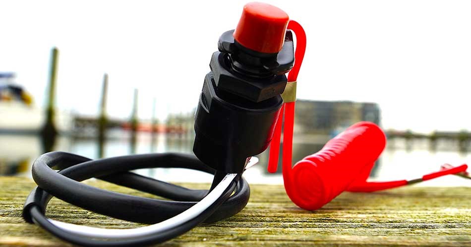 Nødstopsnor/dødmandsknap til båd med rød clips og sort spiral-ledning ligger på en træbro ved havnen.