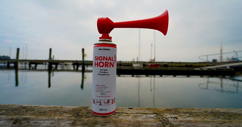 Rød signalhorn fra Biltema placeret på en træbro med vand og havnemiljø i baggrunden.