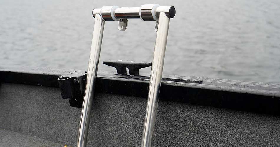 Sammenklappelig bådstige/badestige i rustfrit stål monteret på kanten af en båd, med vand i baggrunden.