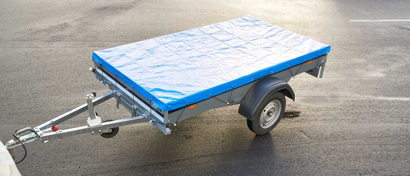 Trailer holdende på asfalt parkering med en trailer presenning på.