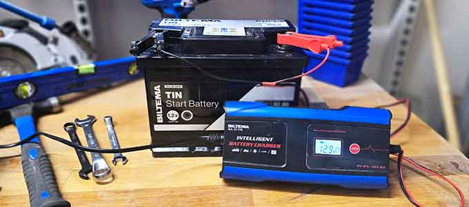 Car battery connected to a charger on a workbench with tools beside