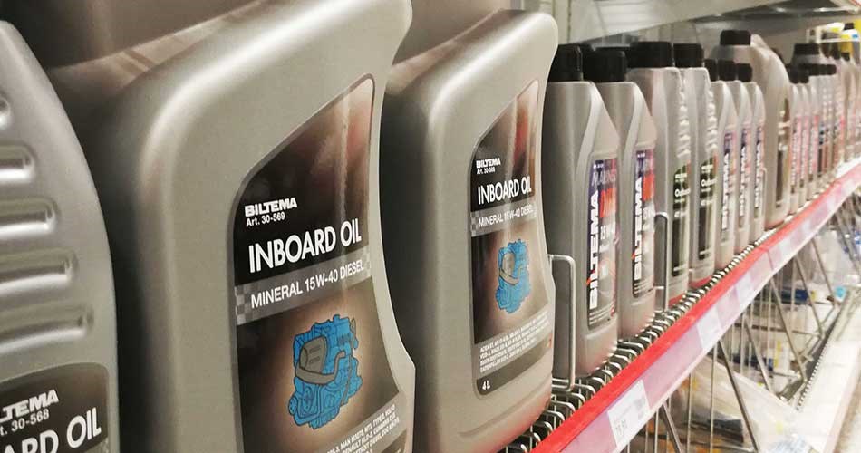 Shelf in Biltema store with rows of Biltema branded motor oil cans for boat engines, with the label showing information about the oil type and viscosity class.