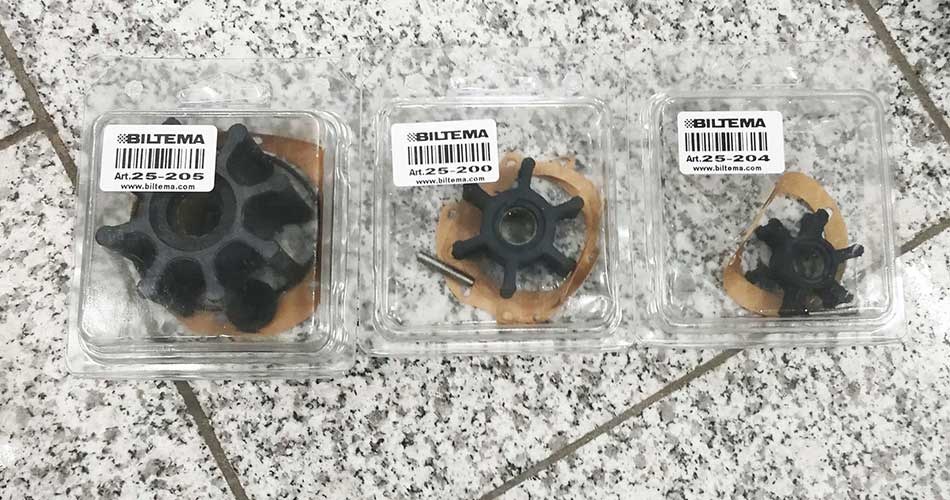 Three different impellers for boat engines packed in clear plastic packaging, placed on a grey mottled tile surface. Each package is labelled with item number and product name.