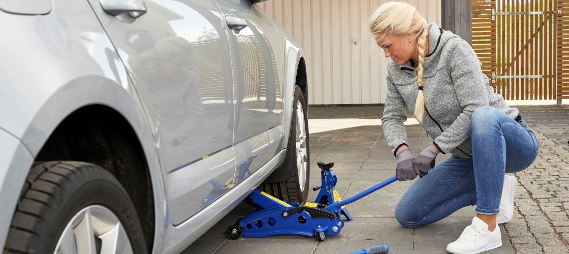 Person changing tyres on car using Biltema jack and wheel wrench in a driveway.