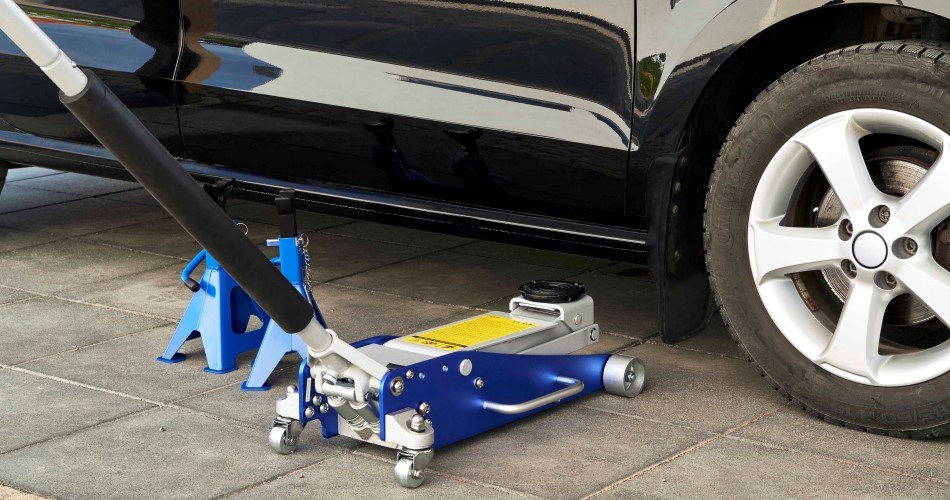 Jack and jack stands used for tyre change on black car parked on tiled surface.
