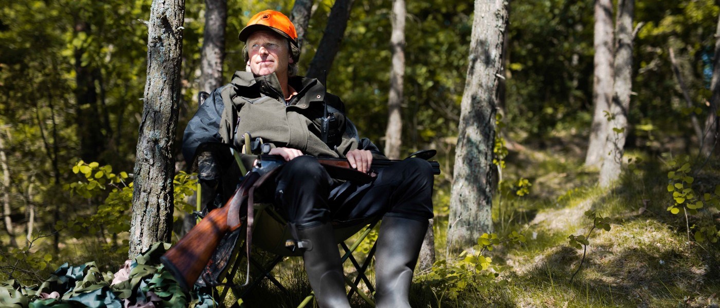 Mand i jagttøj sidder i en jagtstol ude i en skov.