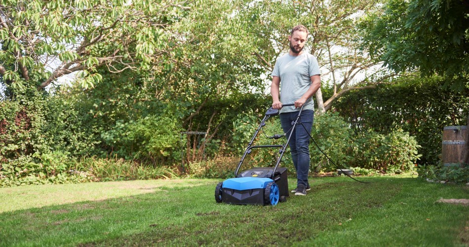 Man walks with a Biltema lawn aerator/vertical cutter in the green surroundings of the garden.