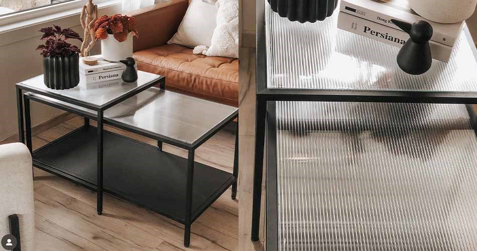 Modern living room with black coffee table with glass top and leather sofa in the background. The right side shows a table surface with an industrial lamp.