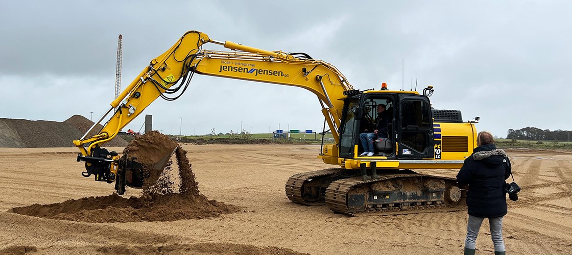Stor gul gravemaskine i arbejde på byggeplads og klar til at tae første spadestik til Biltema Holstebro, under overskyet himmel.