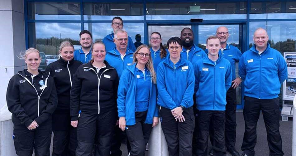 Gruppebillede af Biltema-medarbejdere foran butiksfacade, iført sorte og blå firmatrøjer. Holdet af medarbejdere som åbner Biltema Holstebro.