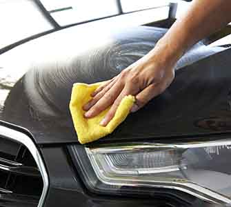 Nærbillede af en hånd, der tørrer en sort bilmotorhjelm af med en gul klud.