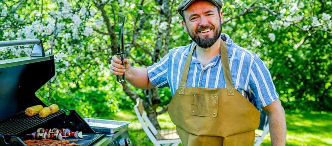 En person som står ved en grill i haven og smiler