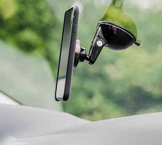 En smartphone sidder i en mobiltelefonholder på indersiden af ​​et bilvindue. Udenfor er frodig grøn vegetation synlig i et slør.