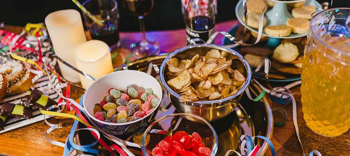 Nytårsbord med chips, slik, drikkevarer, lys og farverige serpentiner.