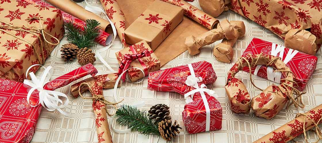 Indpakkede julegaver, gavepapir og julepynt arrangeret på et bord til juleforberedelser.