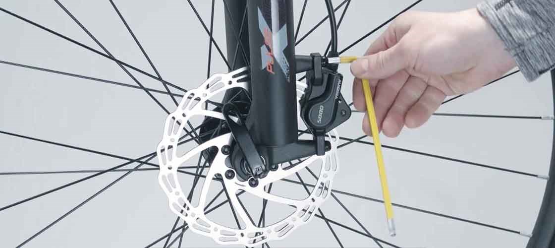 Justering af cyklens skivebremsekaliber med en unbrakonøgle under montering af forhjulet.